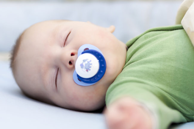 Новорождённый ребёнок сладко спит с синей пустышкой во рту