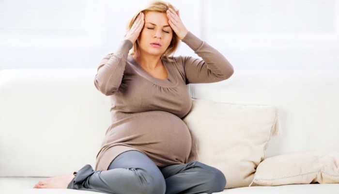 Young pregnant woman sitting on sofa and having a headache.