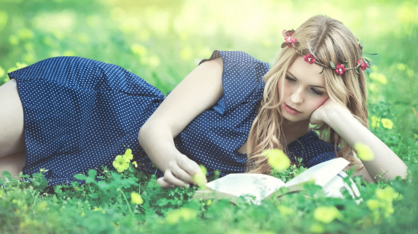 Девушка лежит на траве и читает книгу