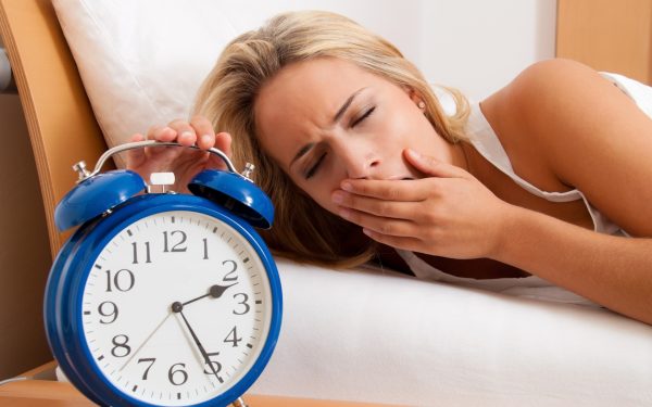 Женщина в постели выключает будильник