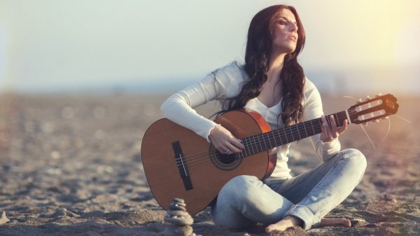 Девушка с гитарой сидит на песке