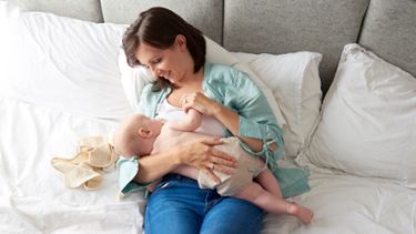 A mother is nursing her baby in the reclined position